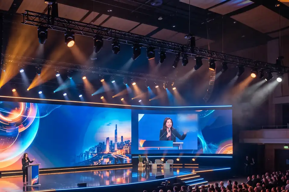 Illustration: a keynote stage with curved LED walls, a camera close-up on screen and moving lights